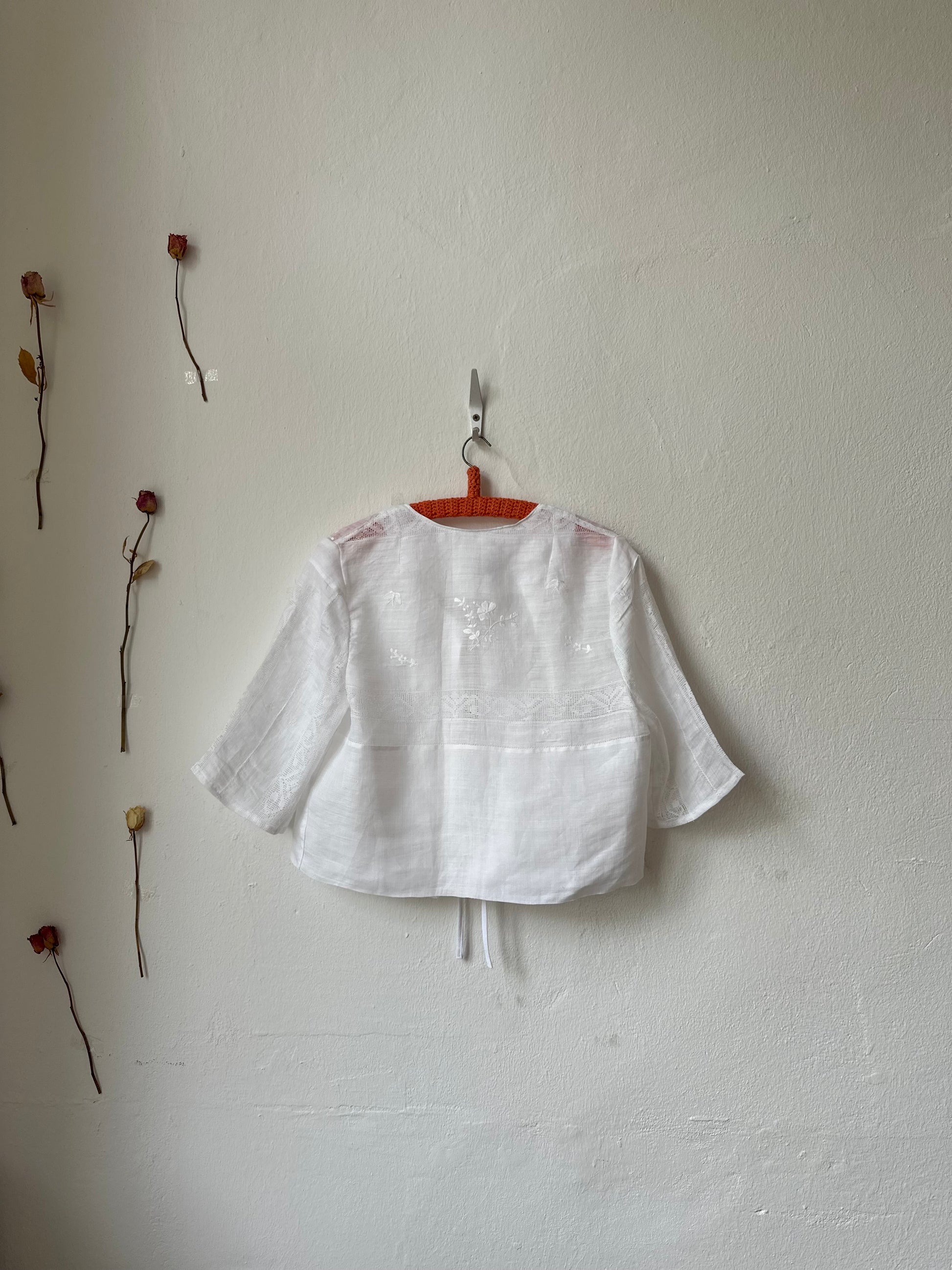 White shirt hanging on a hook against a white wall with dried plants.