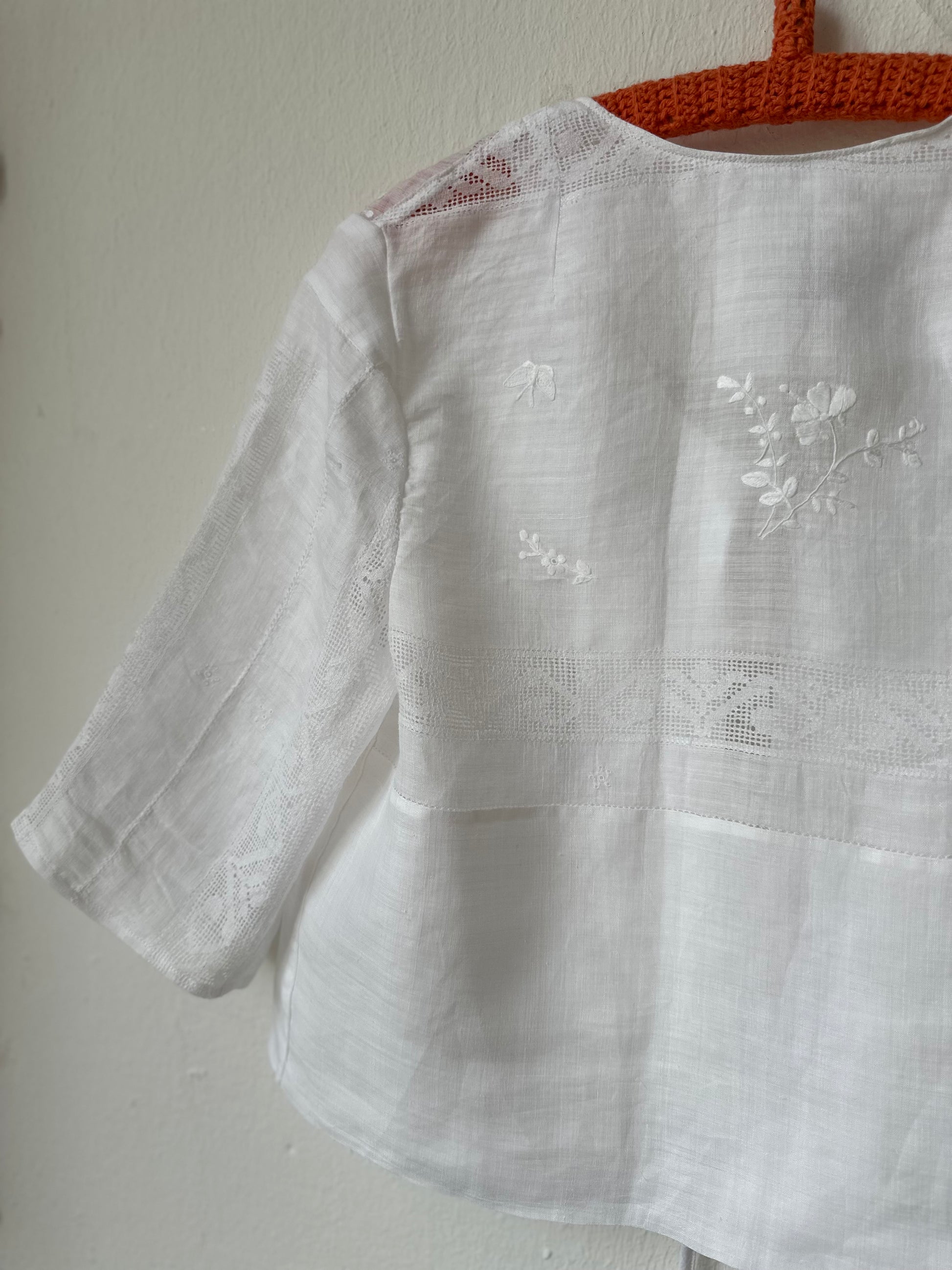White embroidered blouse on a hanger against a plain background
