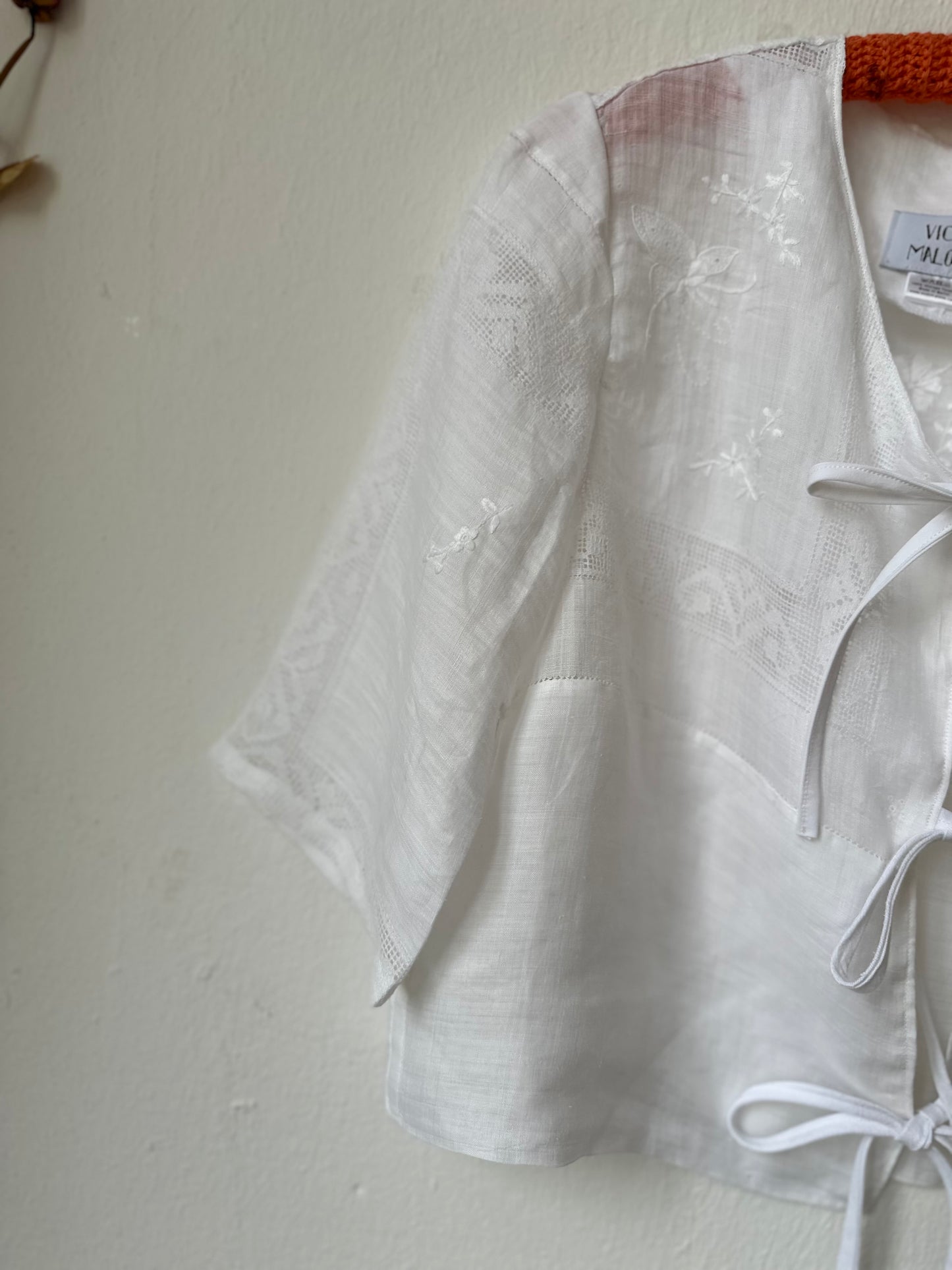 White blouse with lace details on a hanger against a plain wall