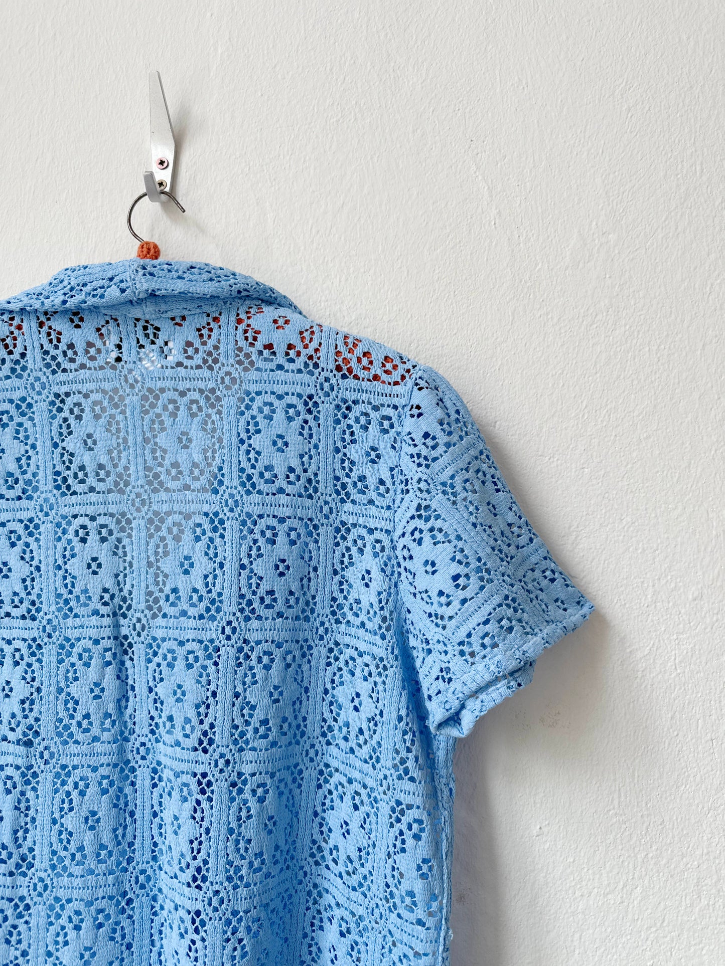Blue lace shirt on a hanger against a white wall