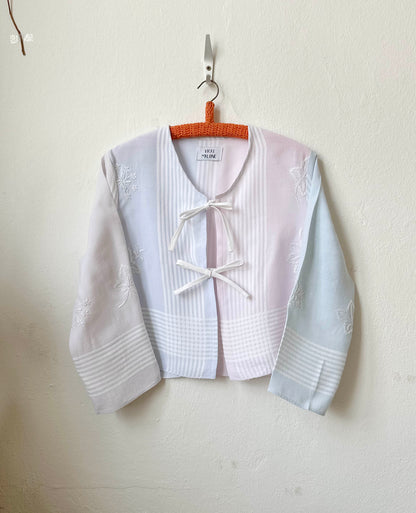 Handmade striped embroidered vintage blouse with long sleeves, made from a Scottish thrift store tablecloth, hanging on a wall
