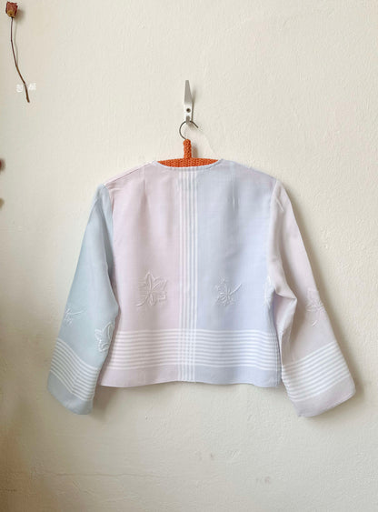 Handmade striped embroidered vintage blouse with long sleeves, made from a Scottish thrift store tablecloth, hanging on a wall
