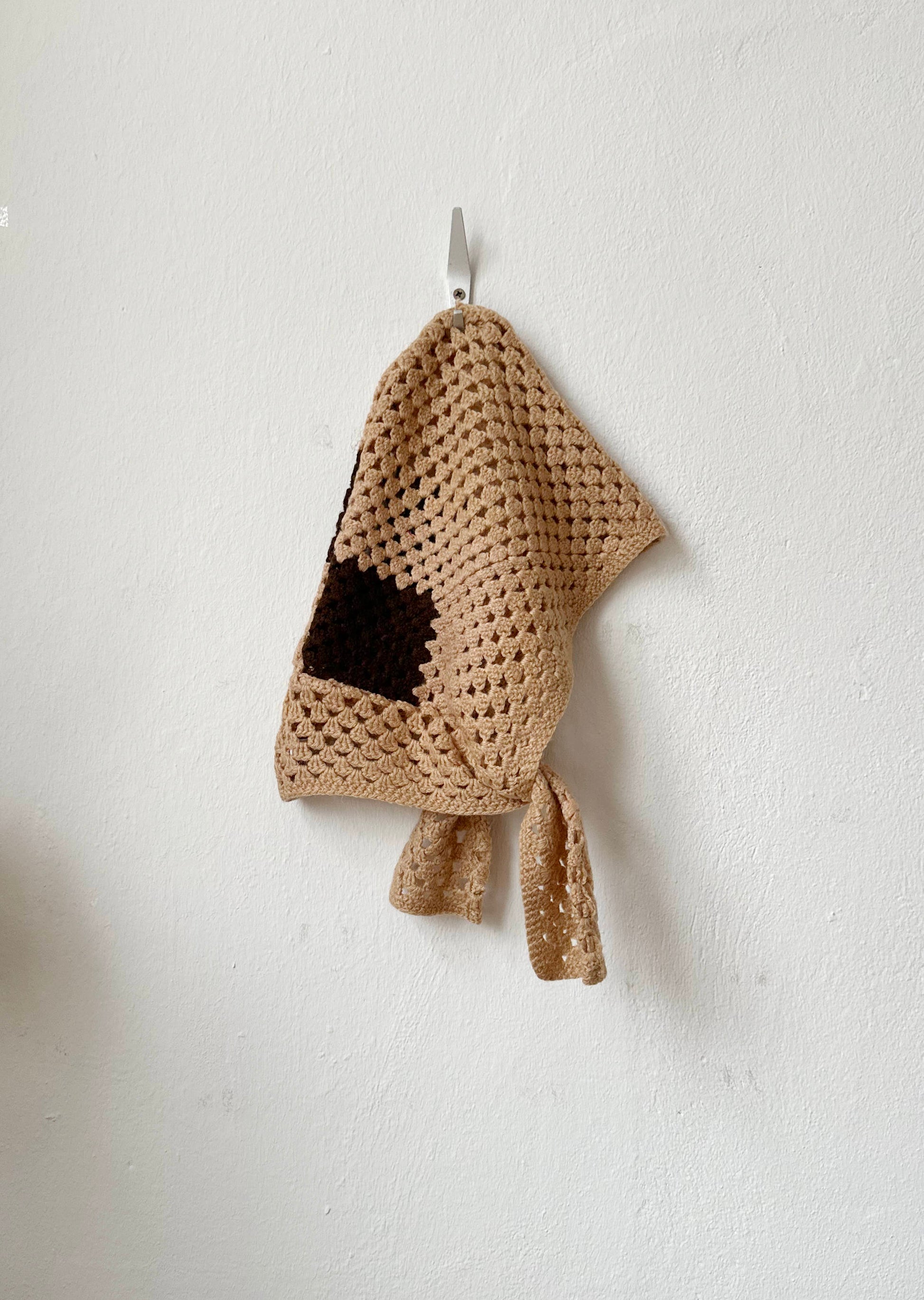 Crocheted beige hood with a brown stripe on a white wall