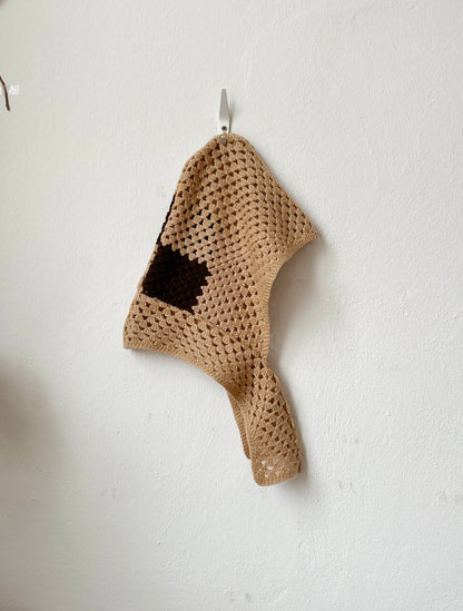 Crocheted beige bonnet hanging on a white wall.