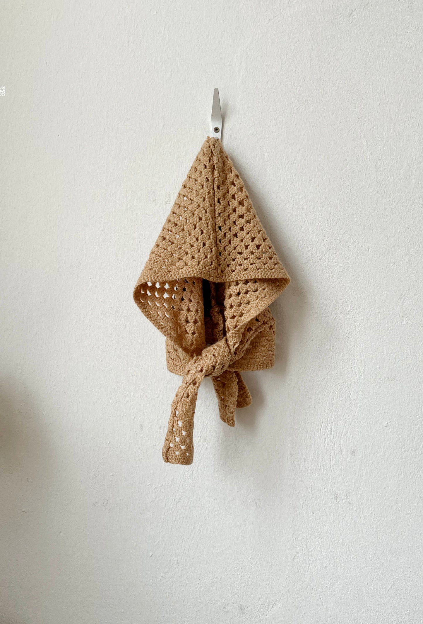 Brown crocheted bonnet hanging on a hook against a light gray wall
