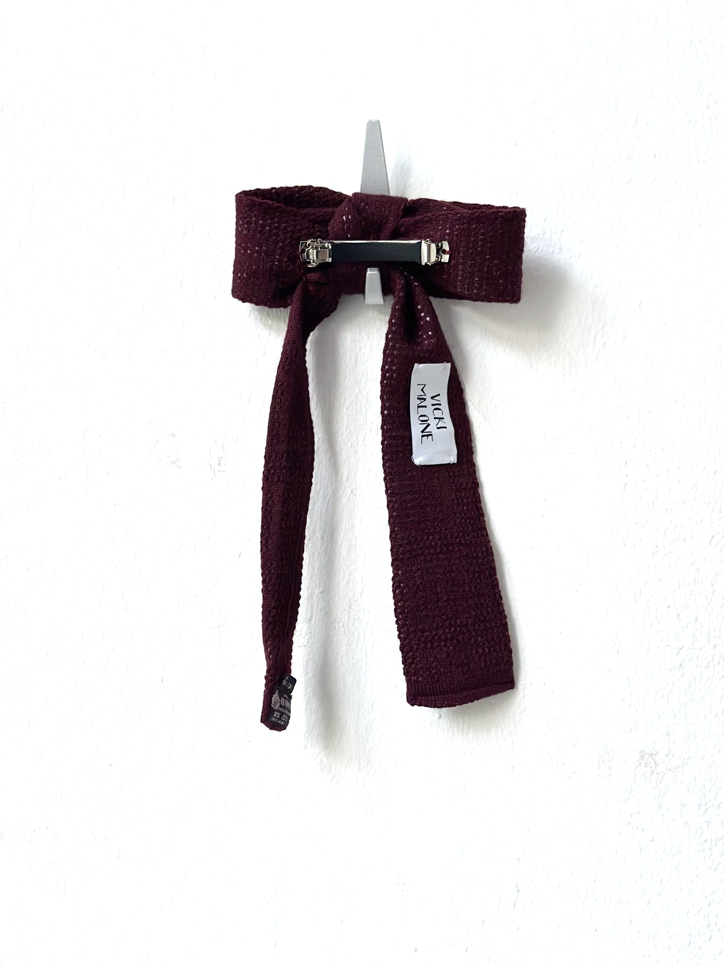 Maroon knitted bow barette with a label on a white background