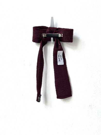 Maroon knitted bow barette with a label on a white background