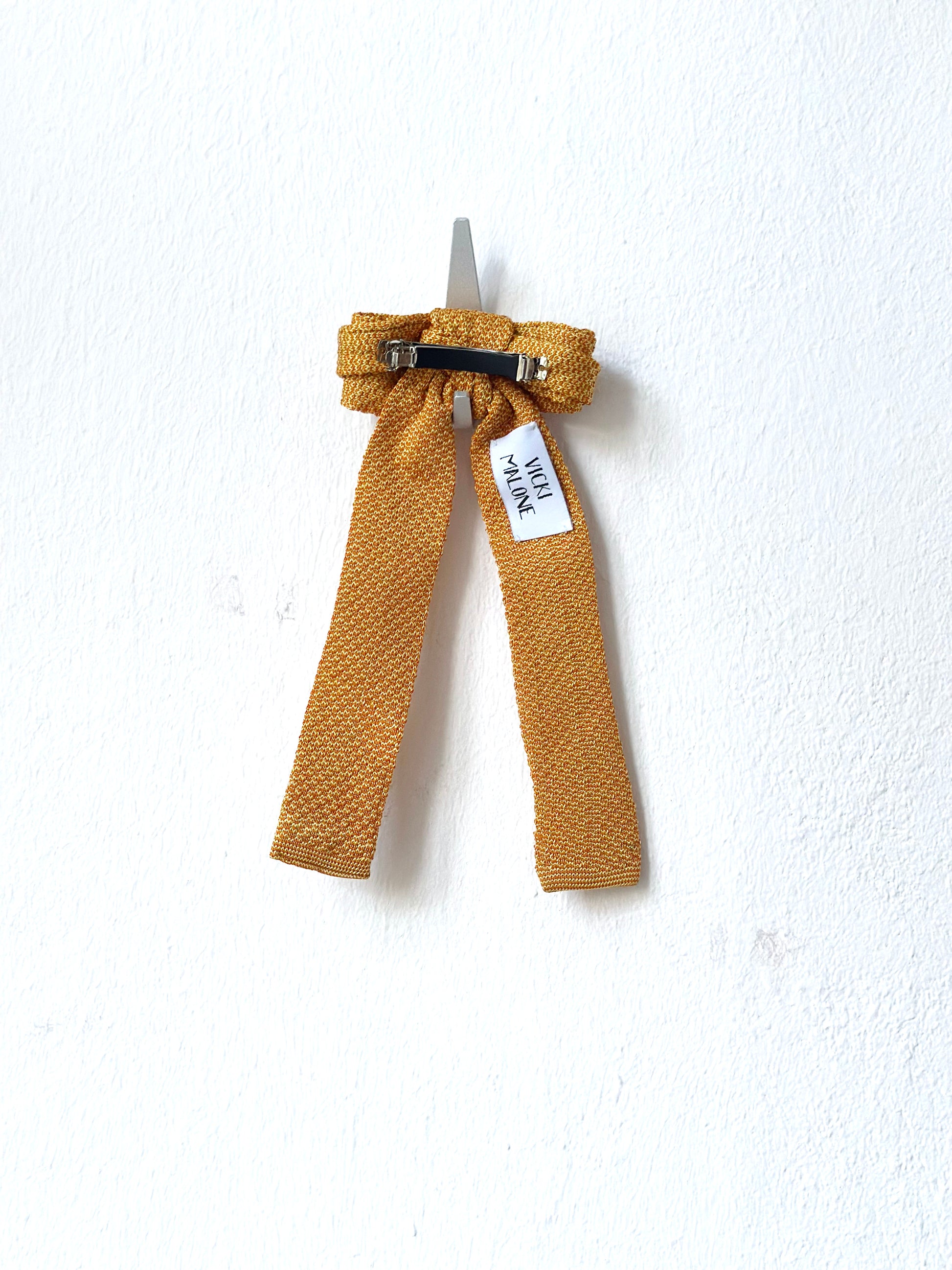 Mustard-colored hair bow with a tag on a white background