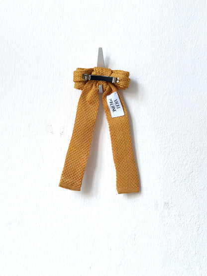 Mustard-colored hair bow with a tag on a white background