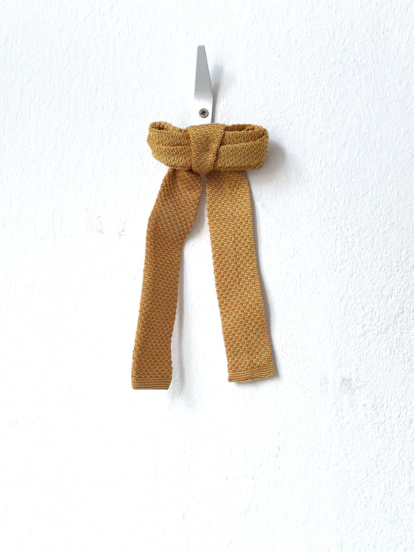 Mustard-colored knitted bow barette on a white background