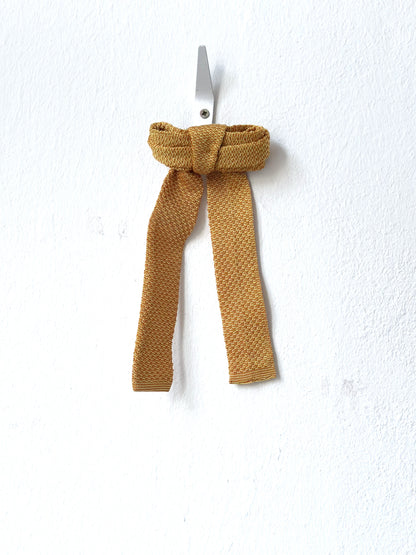 Mustard-colored knitted bow barette on a white background