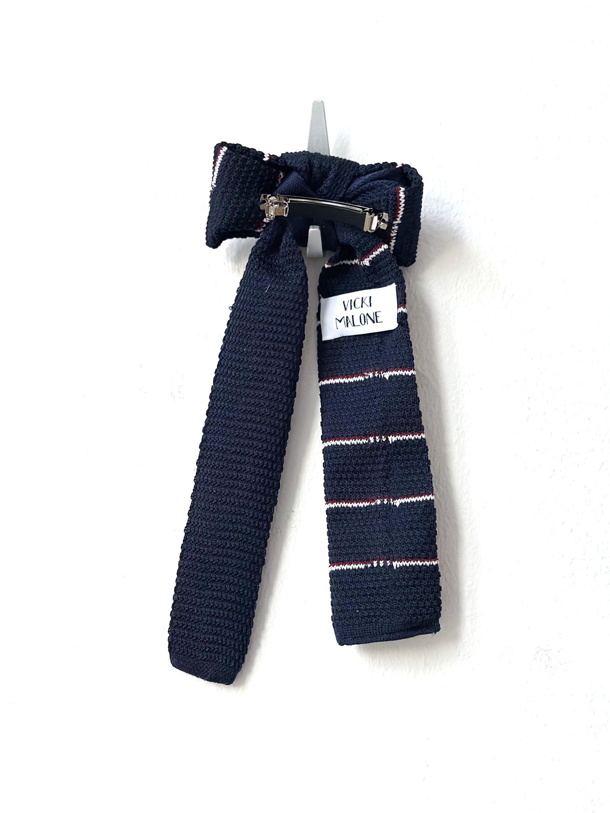 Navy blue knitted bow barette with a white label on a white background