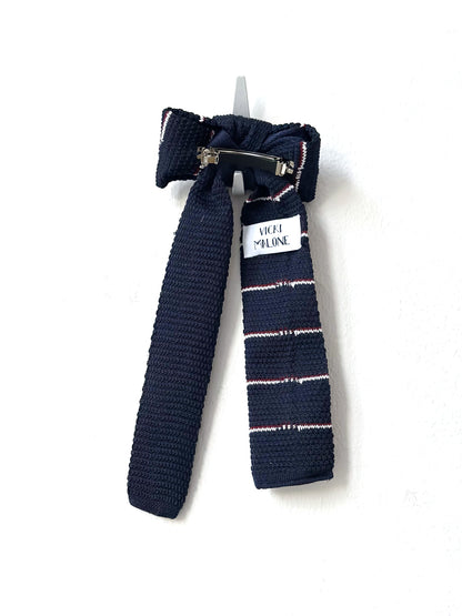 Navy blue knitted bow barette with a white label on a white background