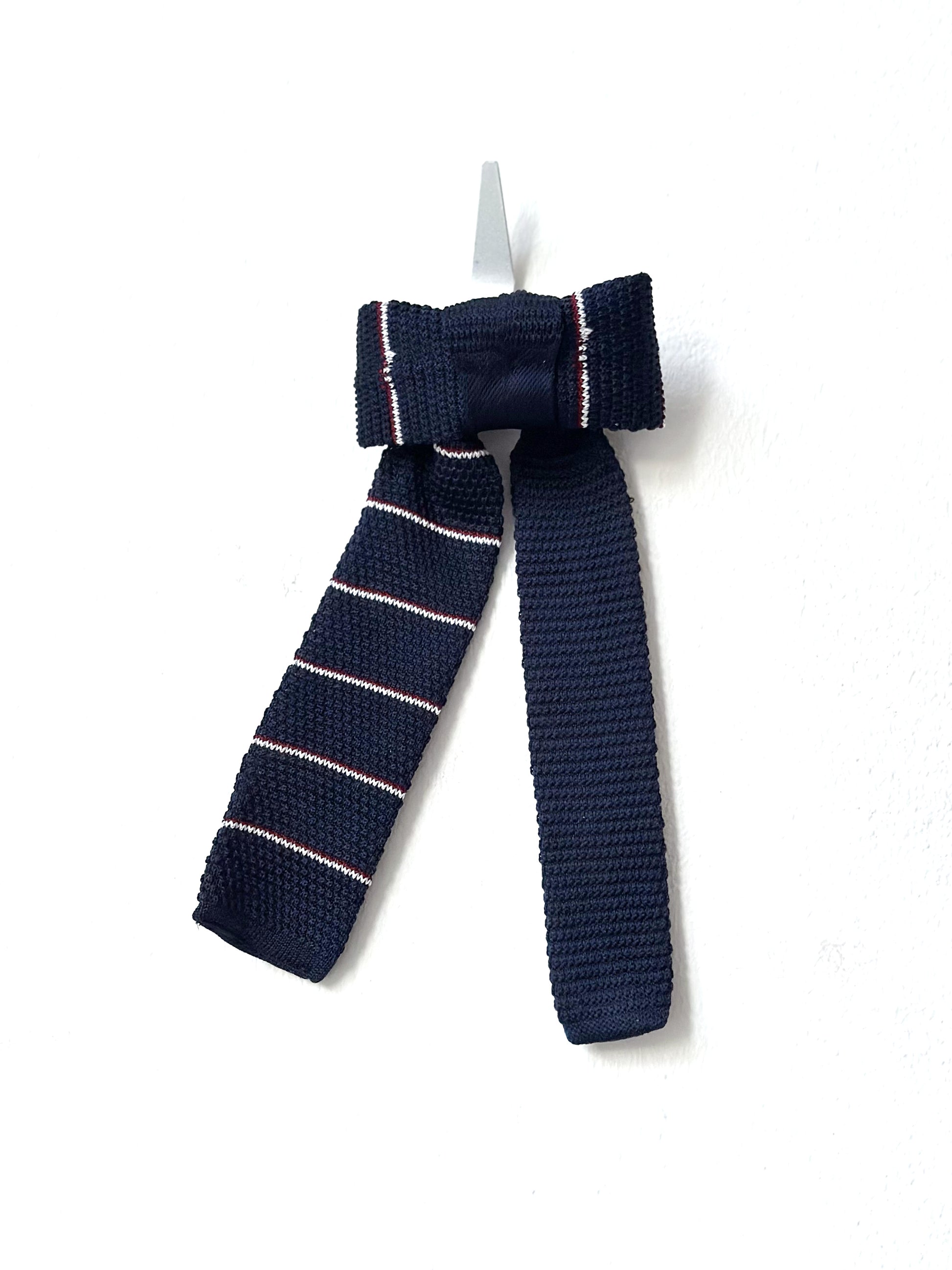 Navy blue knitted bow tie with pink stripes on a white background