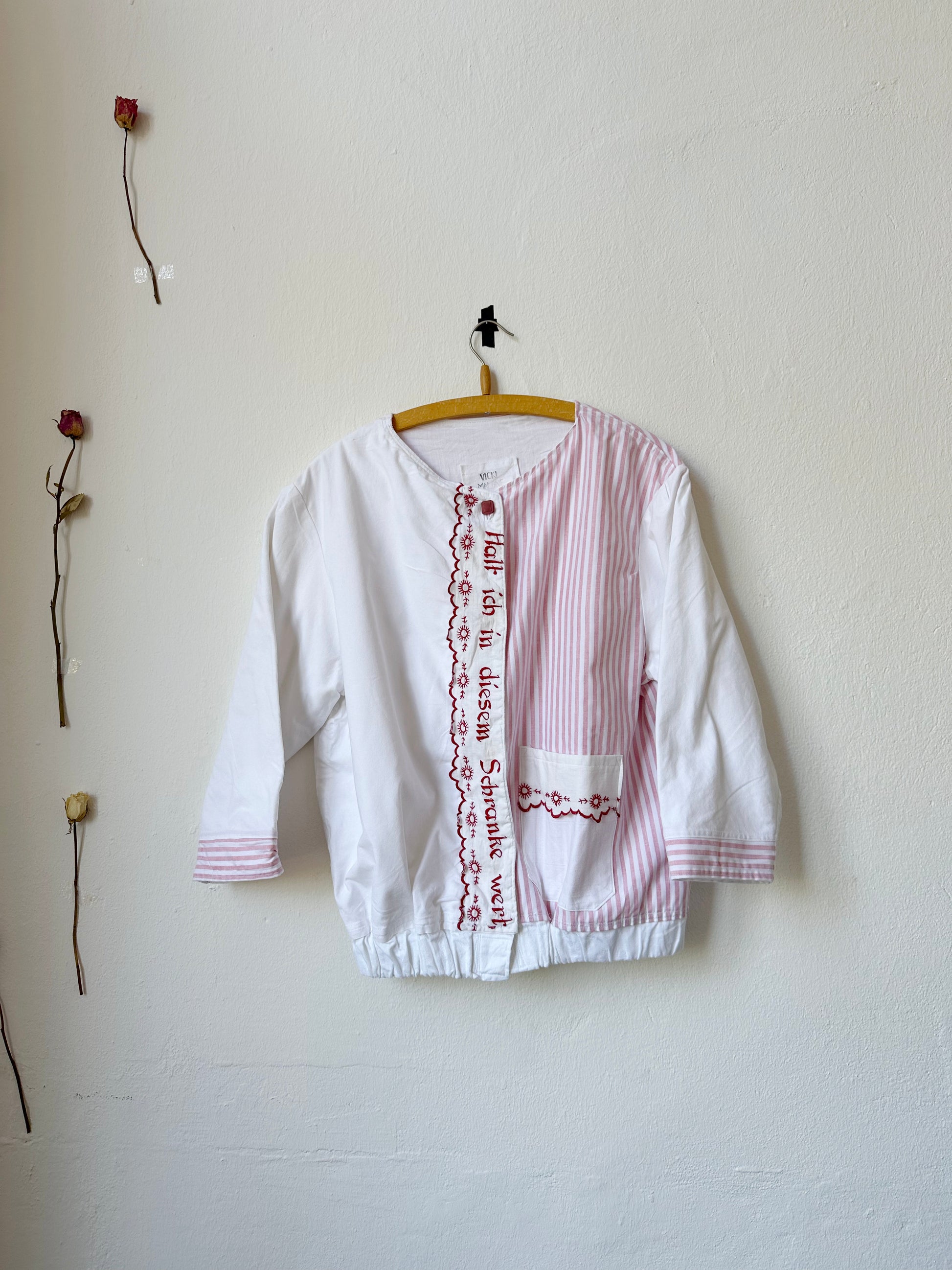 A red and white stripe chore jacket with embroidered german phrases hangs on a wall