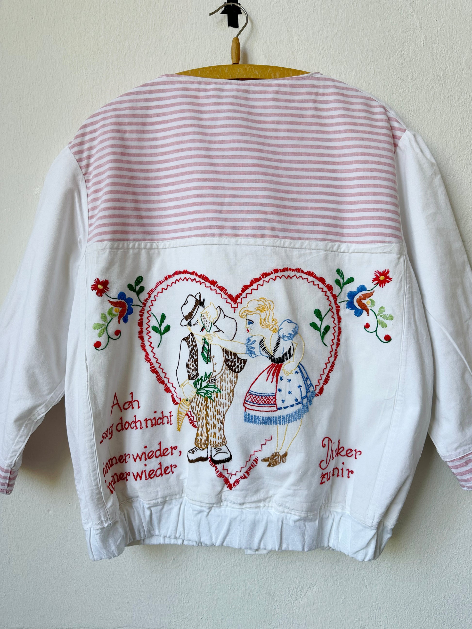 A close up view of a embroidered chore jacket with german phrase and love heart.