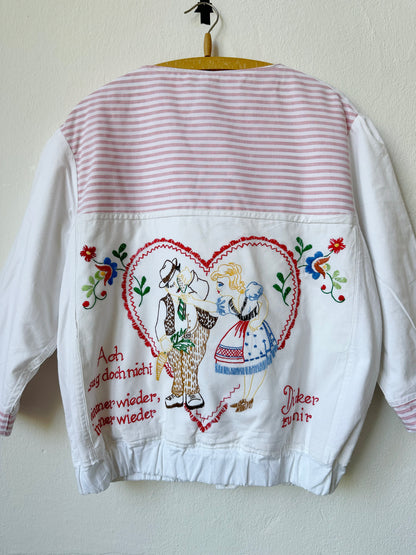 A close up view of a embroidered chore jacket with german phrase and love heart.