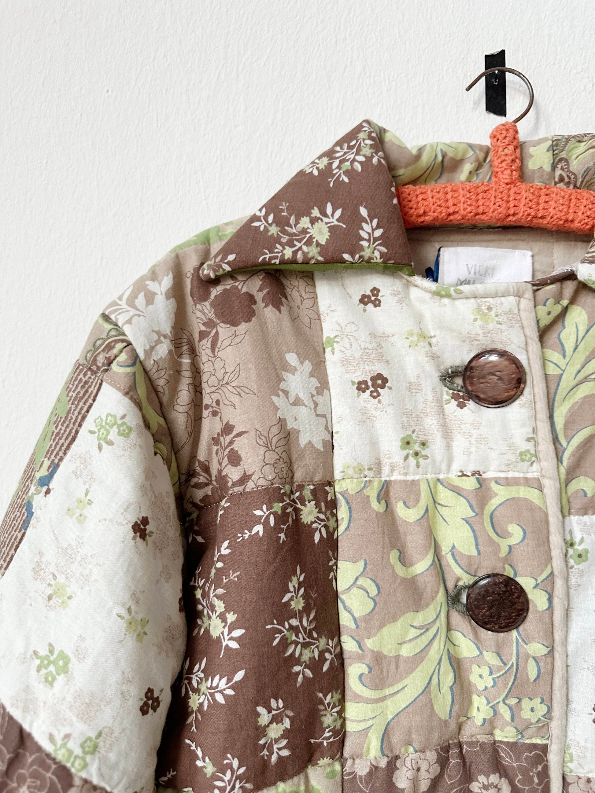 Green and brown patterned quilt jacket with buttons hangs on a wall.