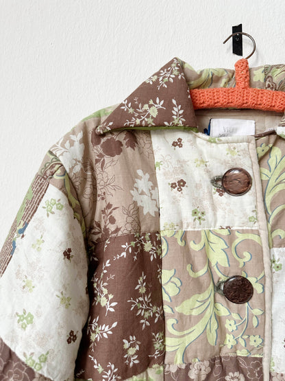 Green and brown patterned quilt jacket with buttons hangs on a wall.