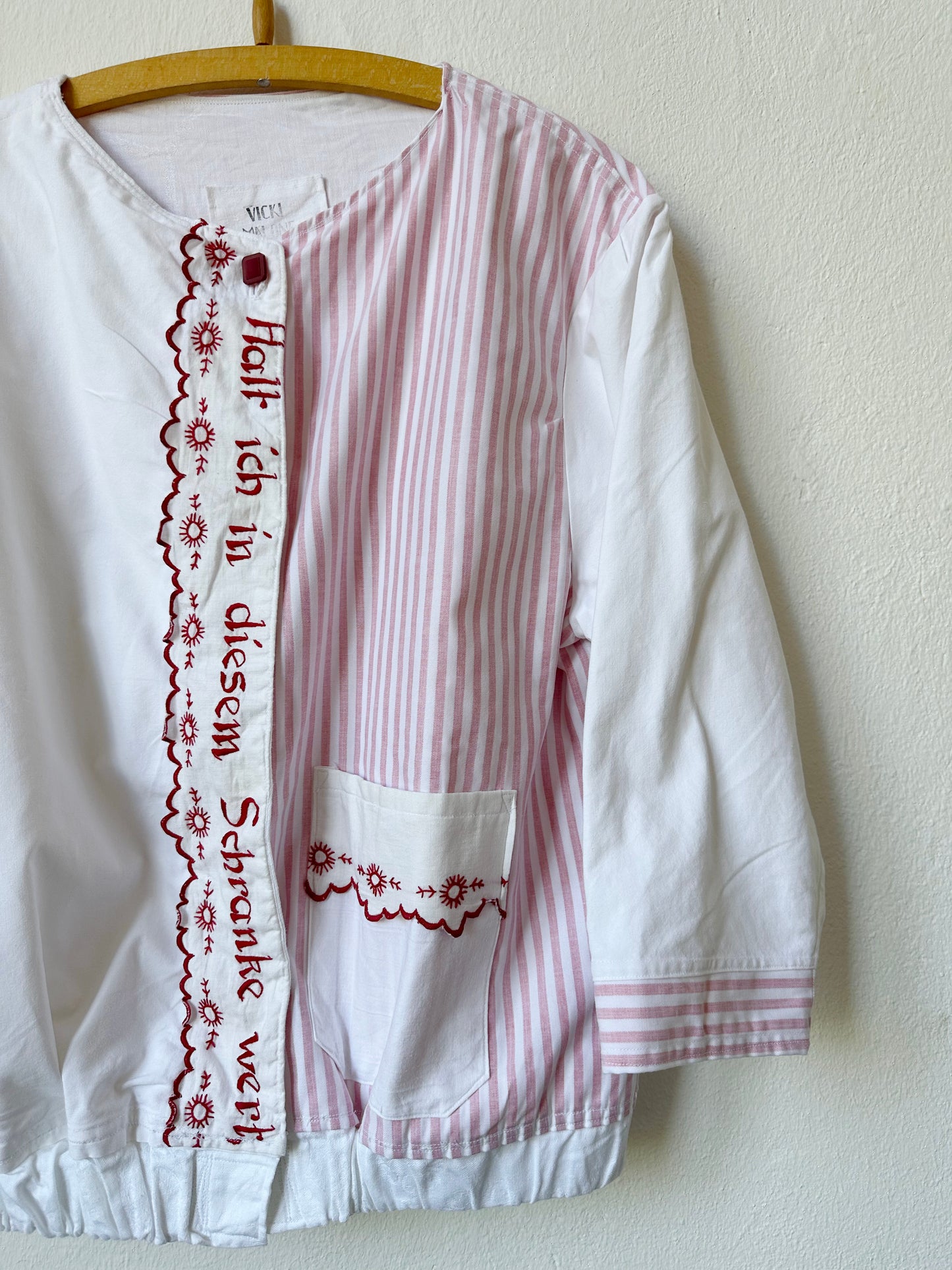 A close up front view of a red and white stripe chore jacket with german embroidered phrases
