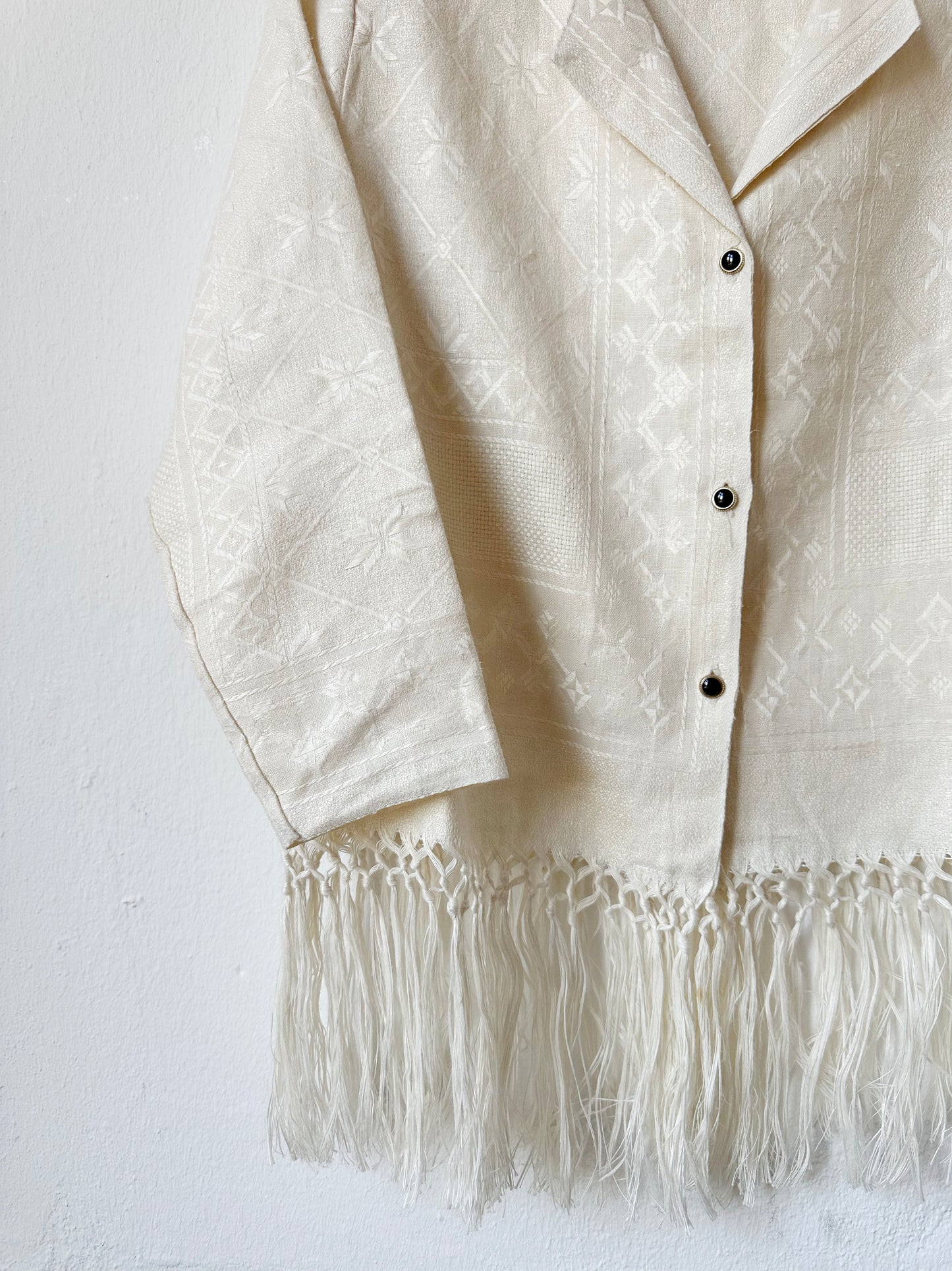 A close up view of the vintage buttons of a blouse with fringed hem hanging on a wall