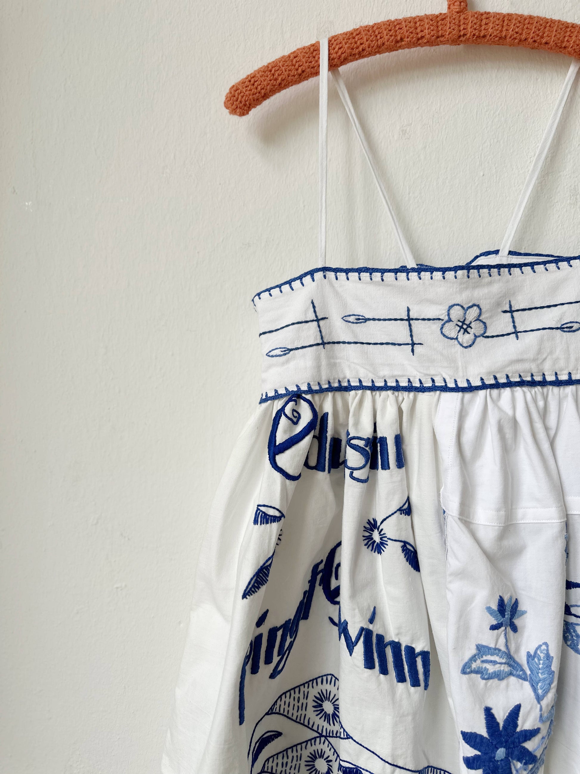 White dress with blue patterns and text on a hanger against a white background