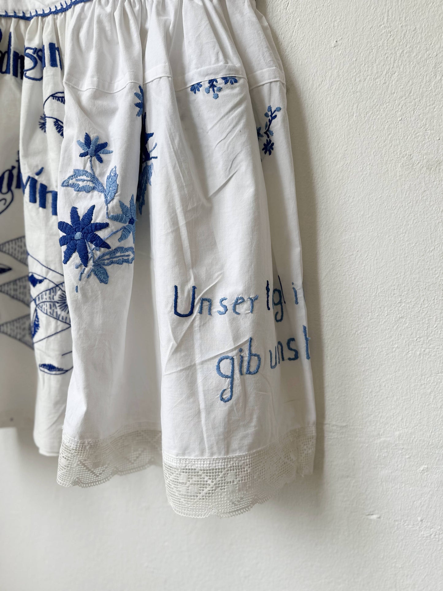 White garment with blue floral and text embroidery on a white background
