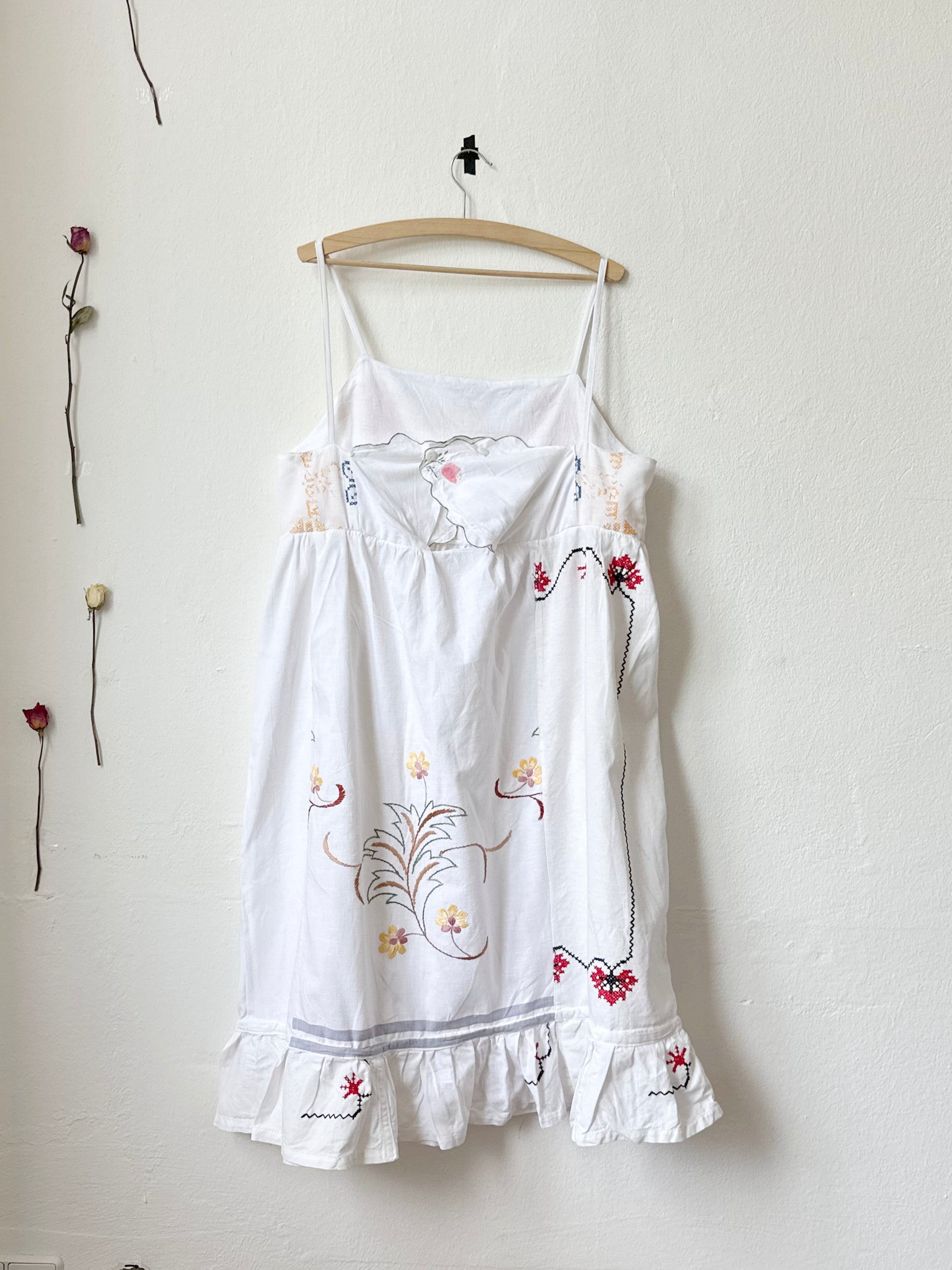 Back view of a white Ellen dress with patchwork details and pockets, displayed on a hanger against a plain wall.