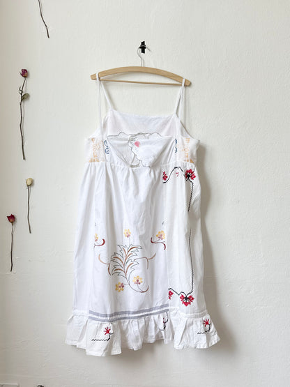 Back view of a white Ellen dress with patchwork details and pockets, displayed on a hanger against a plain wall.