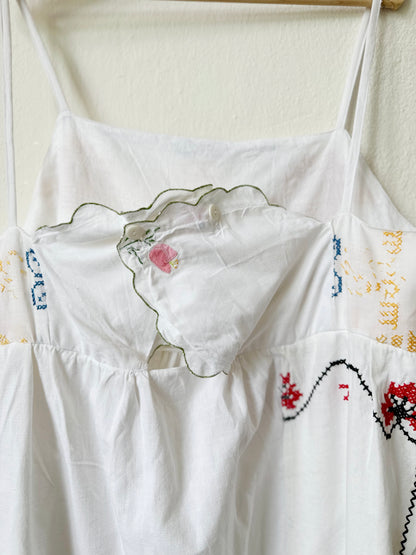 Back detail of a white Ellen dress with embroidered patchwork details displayed on a hanger against a plain wall.