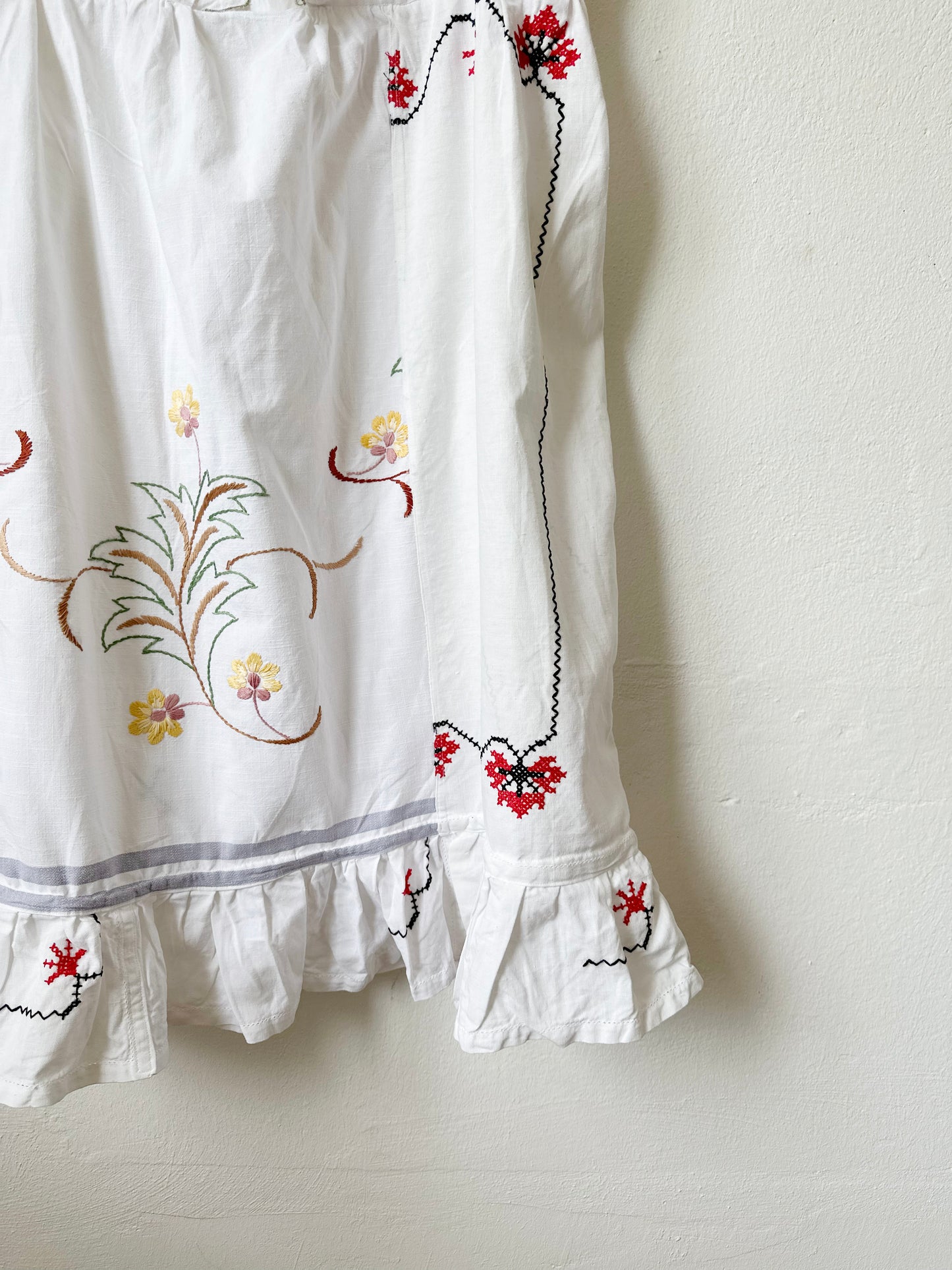 Hem detail of a white Ellen dress with embroidered patchwork details and pockets.
