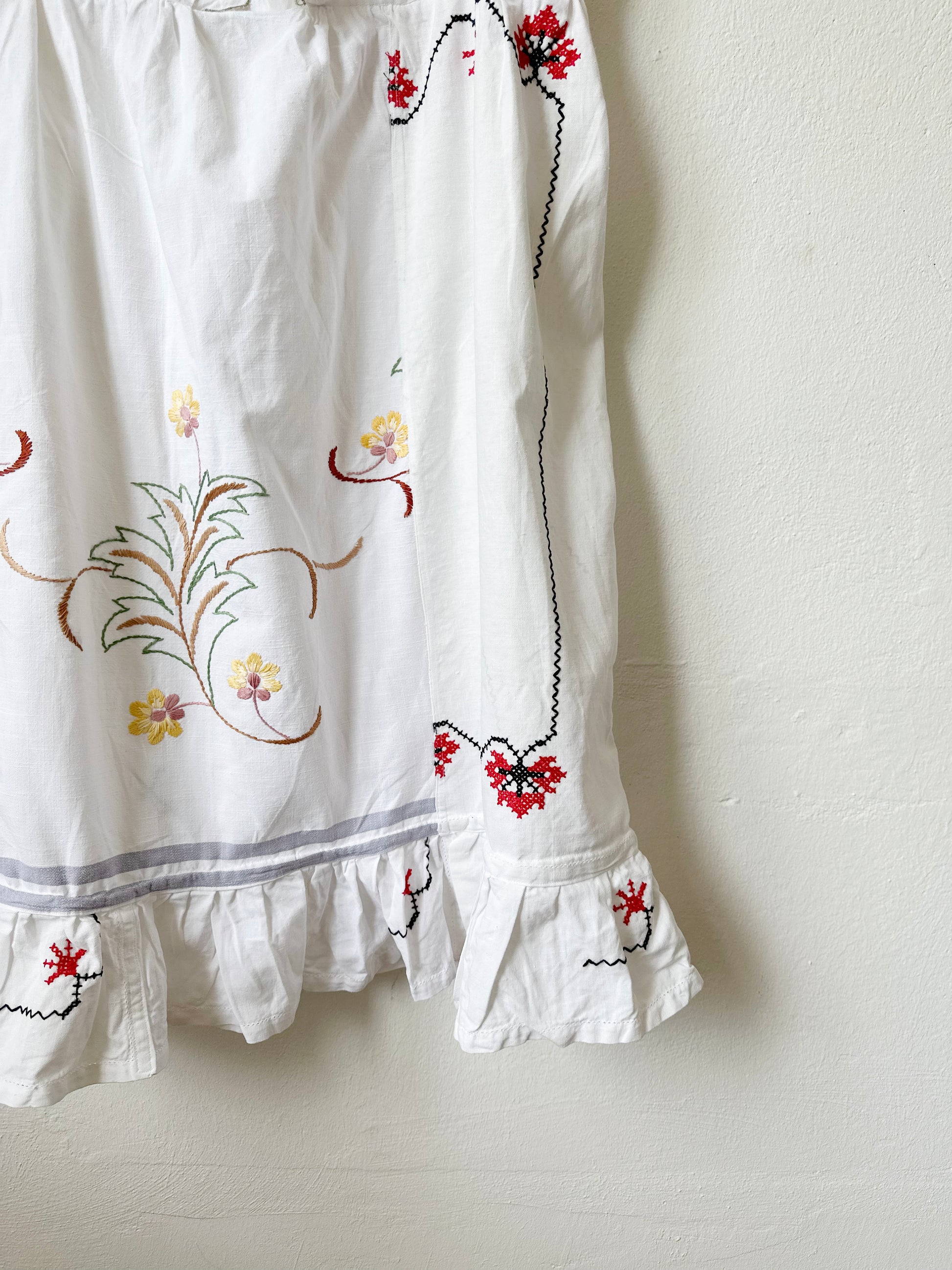 Hem detail of a white Ellen dress with embroidered patchwork details and pockets.