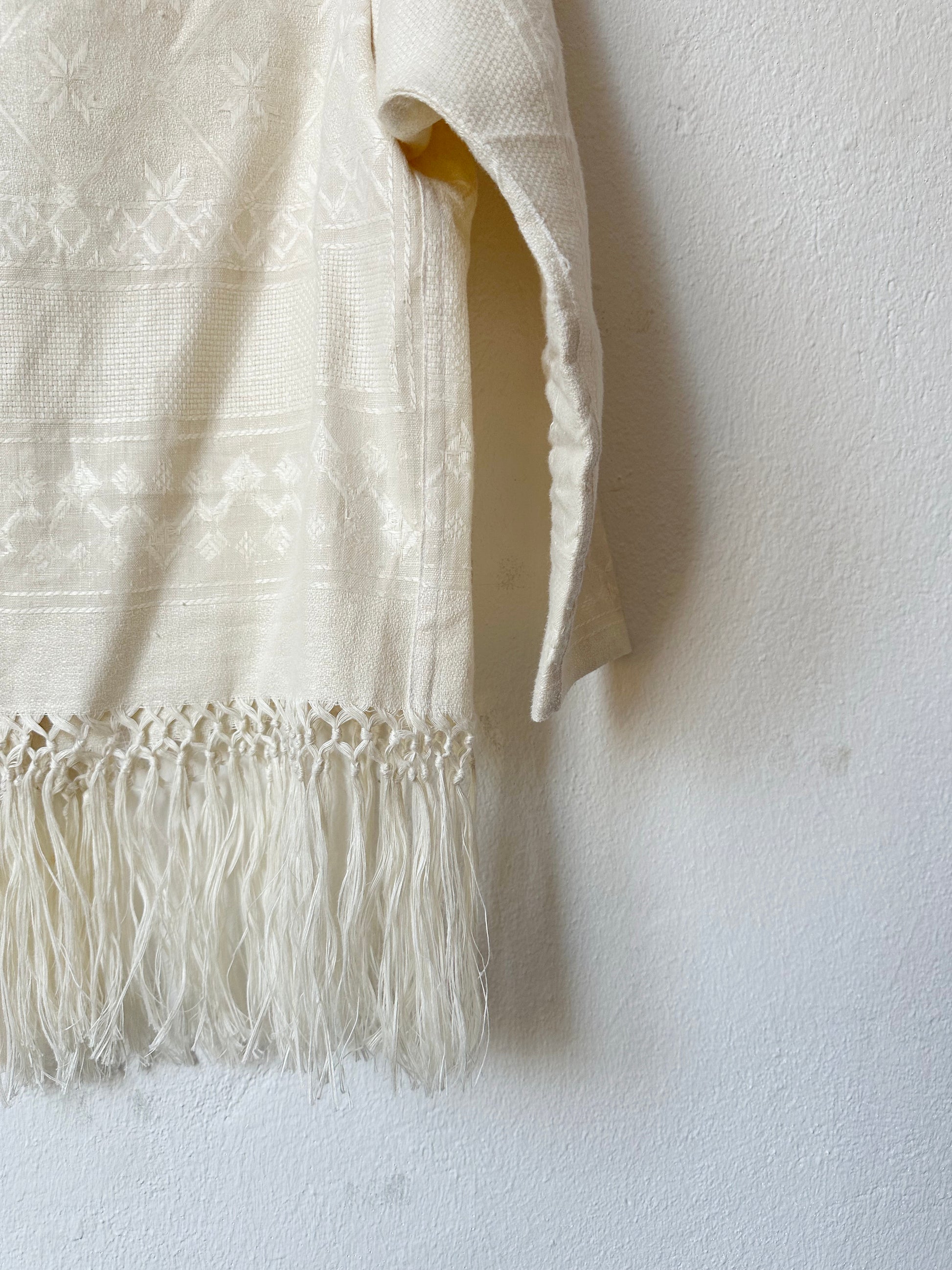 A detail view of the fringed hem of a blouse hanging on a wall