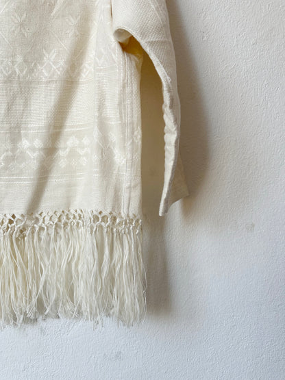 A detail view of the fringed hem of a blouse hanging on a wall