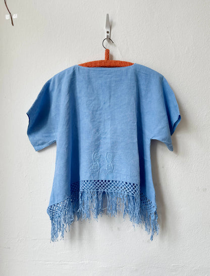 Blue top with fringe on a hanger against a white wall
