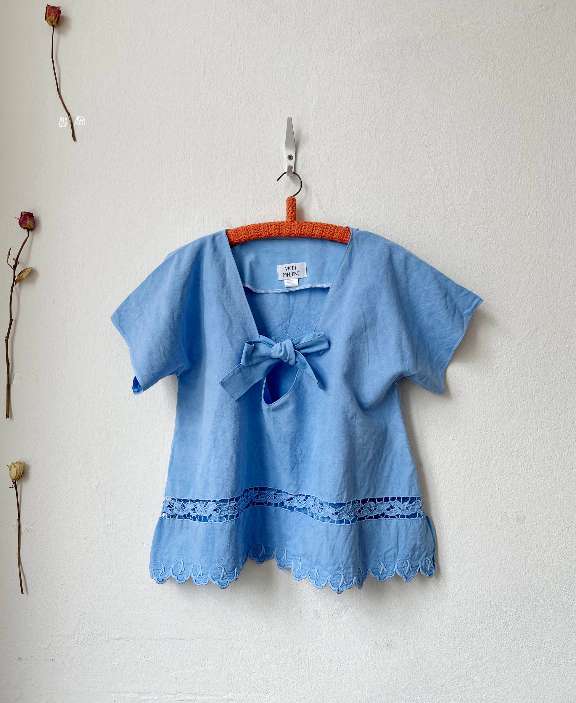 Blue blouse with a bow tie on a hanger against a white wall.