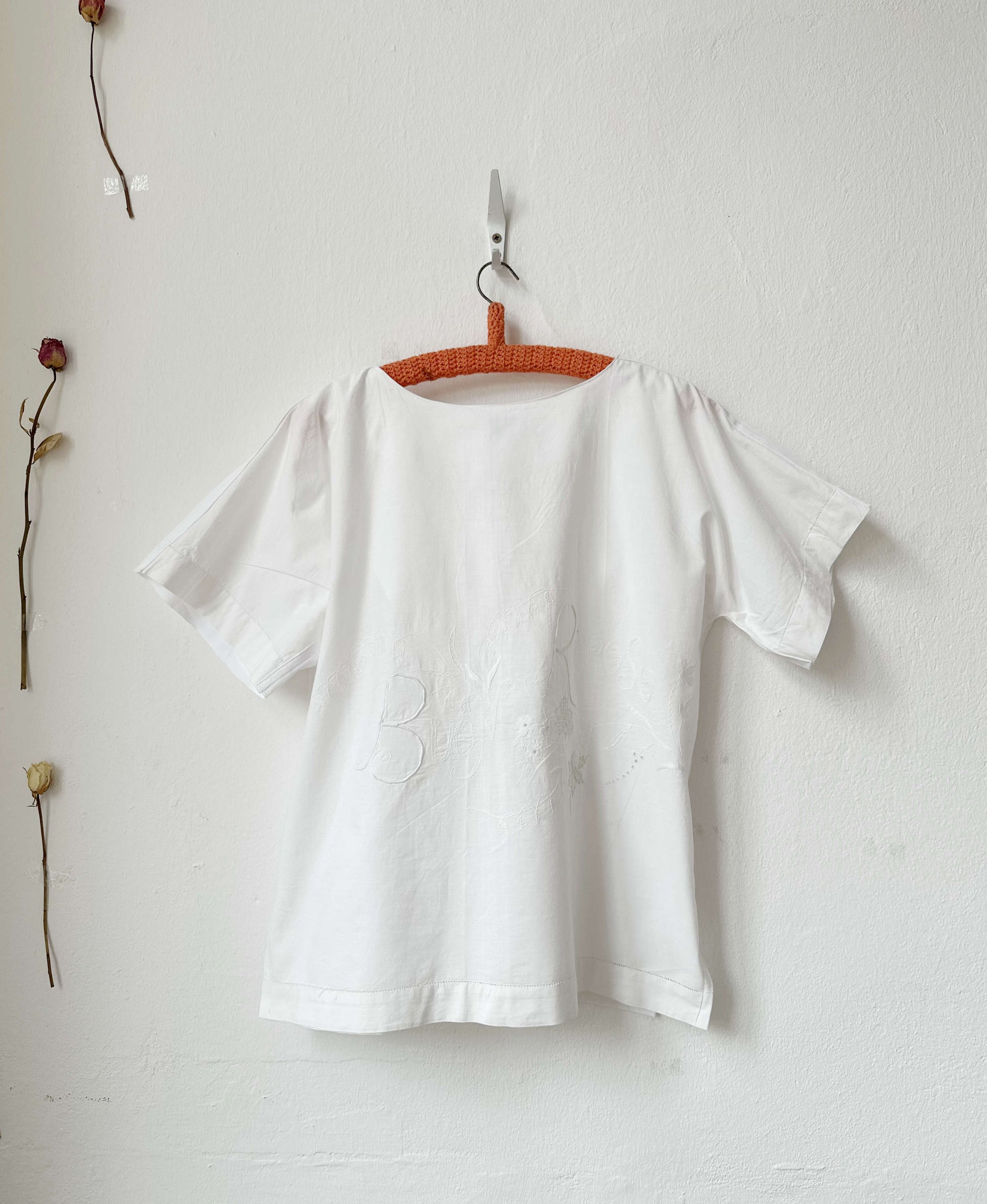 White blouse on a hanger against a plain white wall with minimal decor.