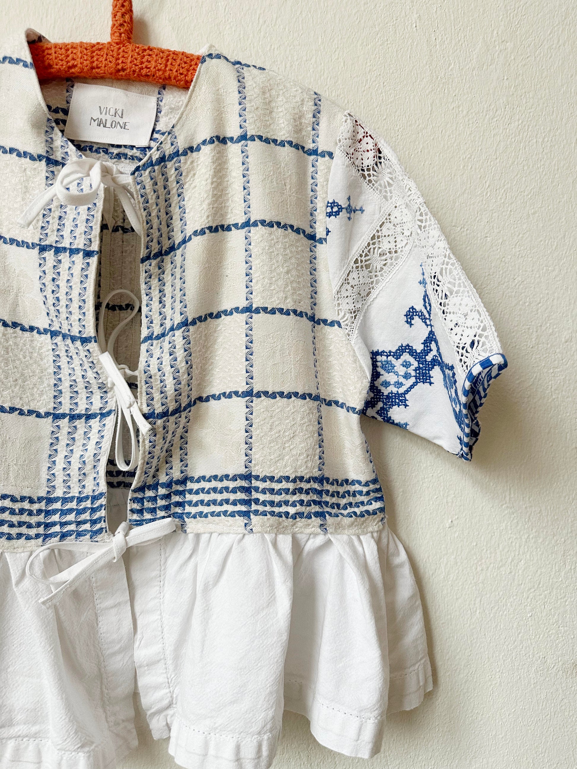 Detailed front view of blue and white check blouse with embroidered sleeve. 