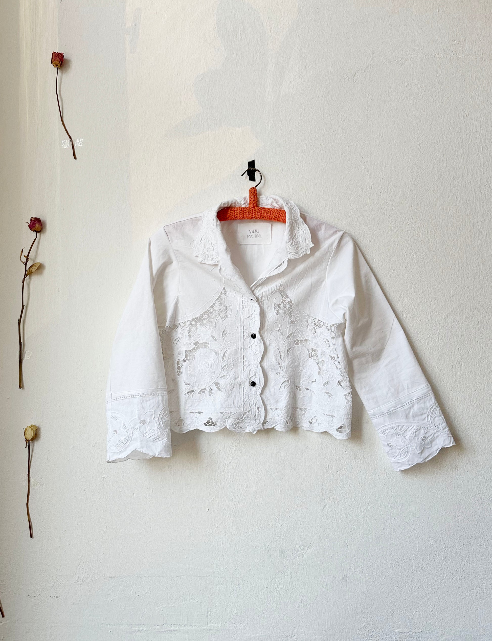 Cropped white lace blouse hangs on the wall. 