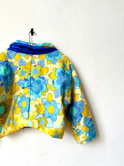 A yellow and blue DDR floral duvet jacket hangs on a white wall.
