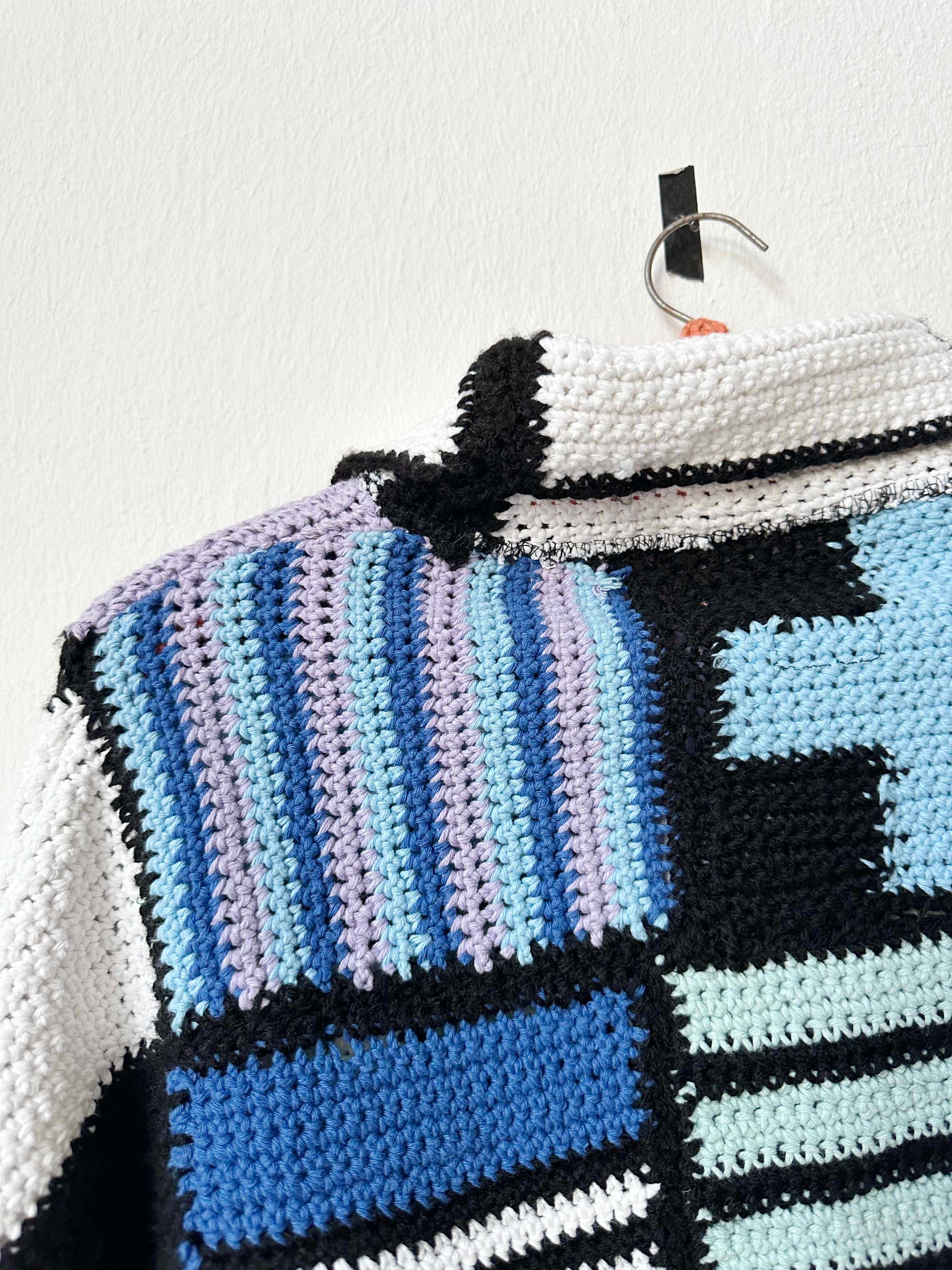 A crochet blanket jacket hangs on a wall.