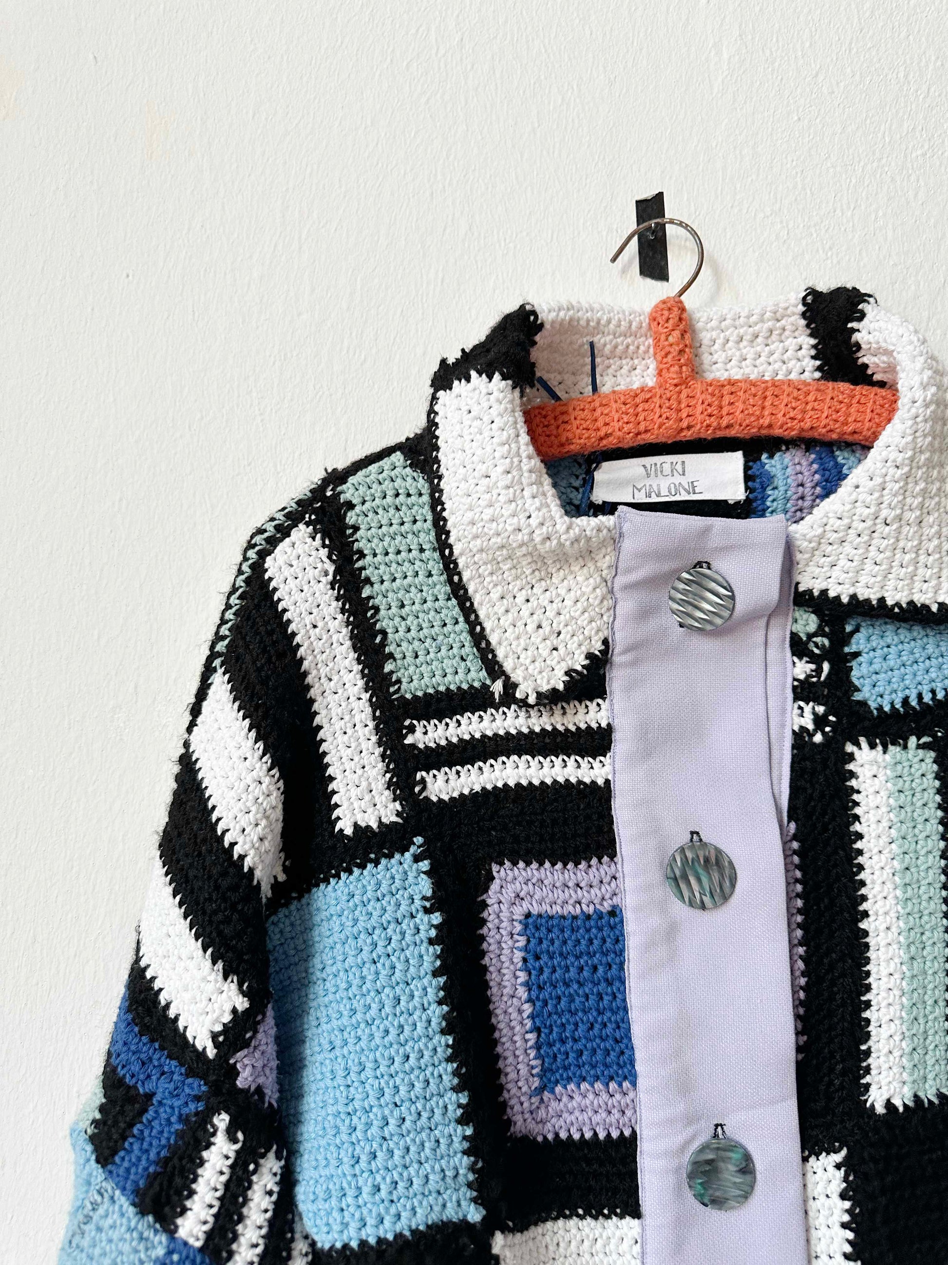 A crochet blanket jacket hangs on a wall.