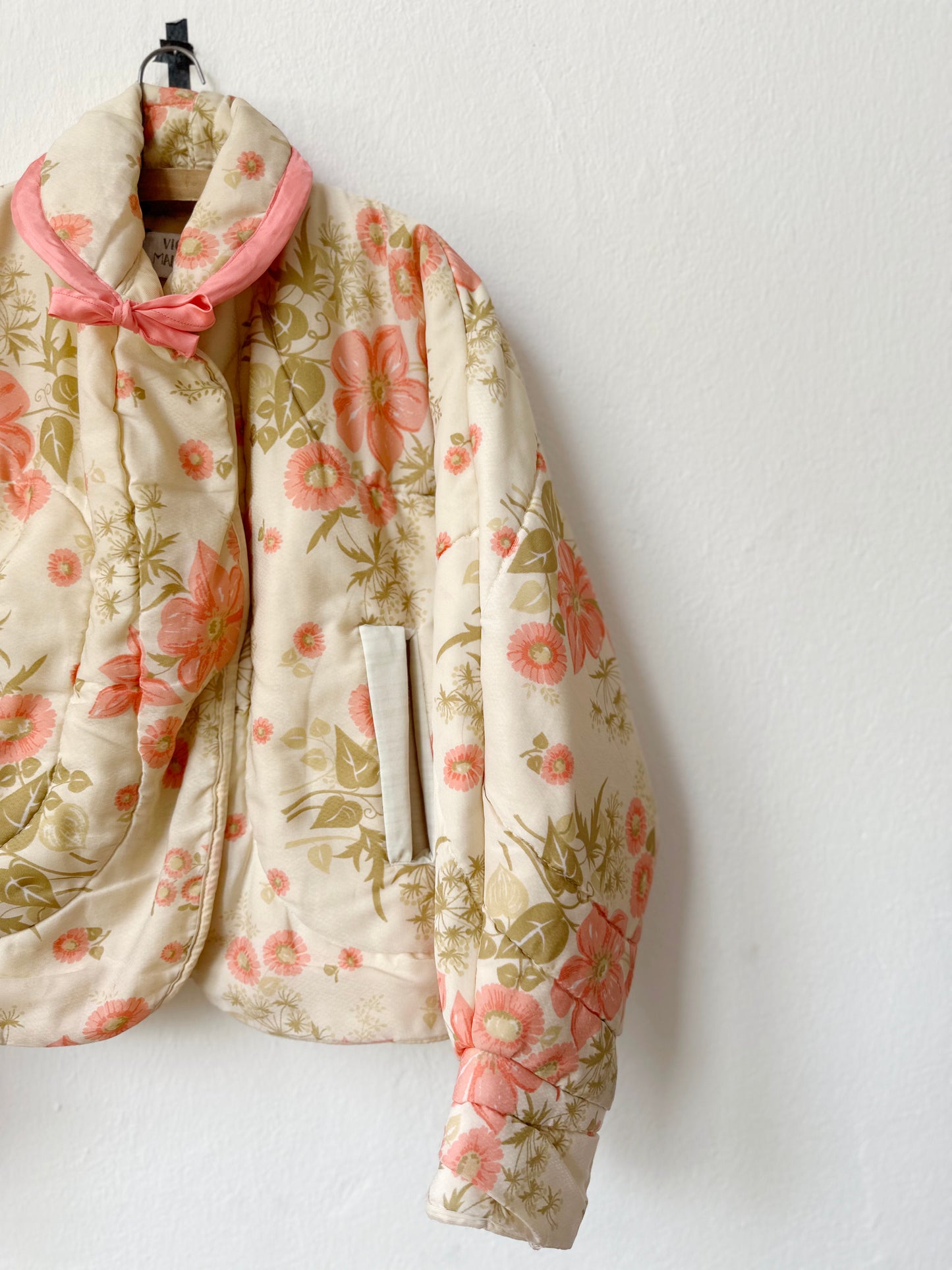 A floral pattern quilt jacket with pockets hangs on a wall.