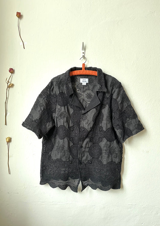 Black lace shirt hanging on a hook against a white wall with a dried flower.