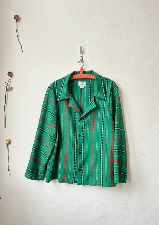 Green and red striped shirt hanging on a white wall with minimal decor.