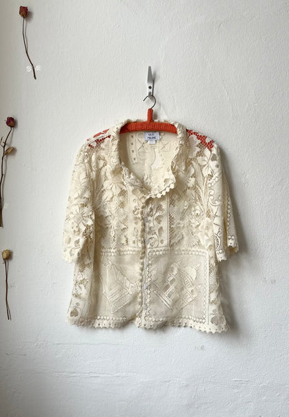 Cream lace blouse hanging on a hook against a white wall.