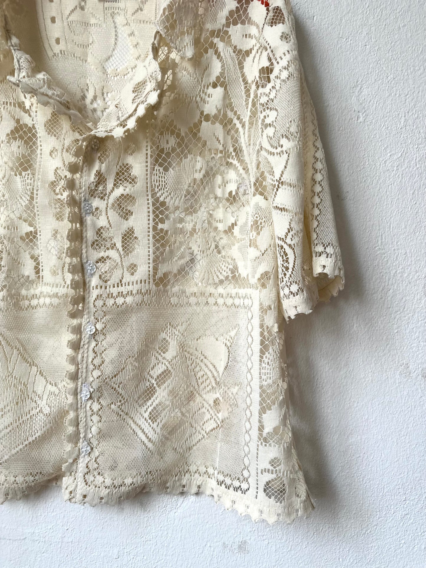 Detailed lace shirt on a white wall.