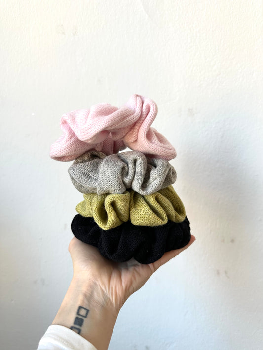 Hand holding four colourful scrunchies against a white background