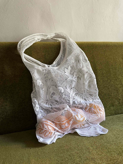 A white floral lace tote bag draped on an olive green velvet sofa against a light beige wall.