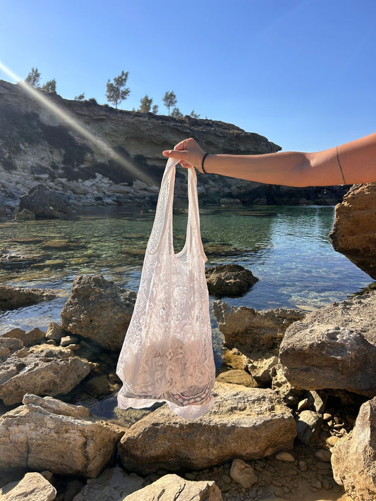 A lace tote bag held over rocks at the beach.